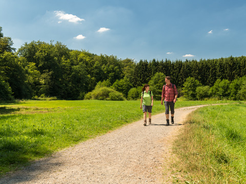 Wandern am Eifgenbachweg Zwei Wanderer auf einem sonnigen Waldweg in Wermelskirchen, umgeben von grüner Natur.