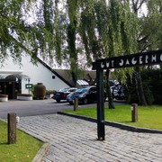 Steakhaus Gut Jägerhof in Erkrath Eingangsbereich des Gut Jägerhofs mit gepflastertem Weg, umgeben von grünen Bäumen und parkenden Autos.