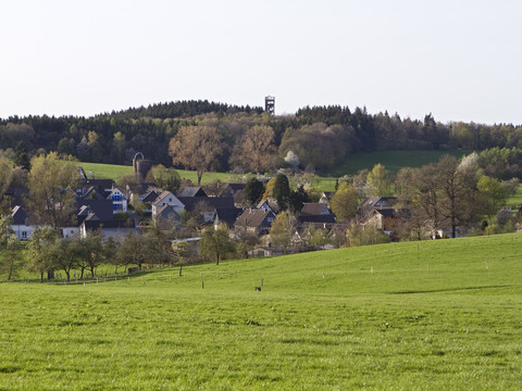 Wanderung zwischen Benroth und Ödinghausen Dorf Nümbrecht eingebettet in grüne Wiesen und Wälder, im Hintergrund ein Aussichtsturm.