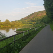 11_hx_zbih_weserradweg_wuergassen_stephanberg.jpg Radweg entlang eines Flusses mit bewaldetem Hang im Hintergrund und üppiger Vegetation.