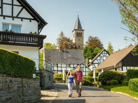 Seelscheid <p>Pärchen spaziert durch ein idyllisches Dorf mit Fachwerkhäusern und Kirchturm im Hintergrund.</p>