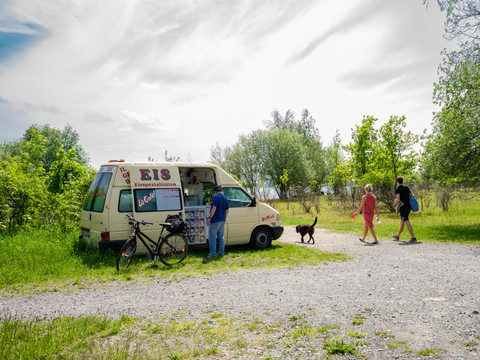 Am sommerlichen Cospudener See steht ein Eiswagen, darum spazierende Menschen mit Hund und Fahrrad, Sommer, Freizeit, Region, Leipziger Neuseenland