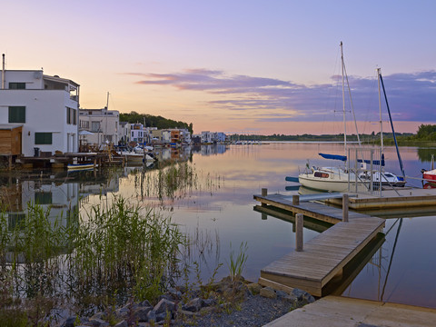 Idyll at Lake Hain A calm lake at sunset, lined with modern white houseboats and sailing boats moored in the bay.
