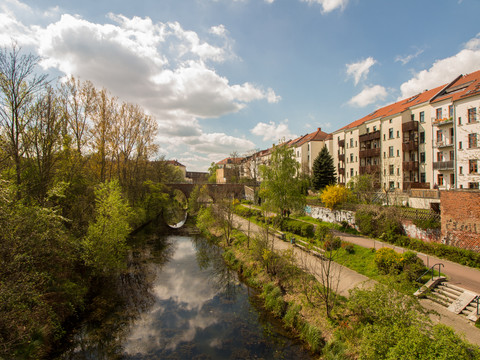 Kanál Karla Heineho - Vody v Lipsku Der Karl-Heine-Kanal im Frühjahr, umgeben von grün werdenden Bäumen, mit einer Brücke und auf der rechten Seite Wohnhäusern mit Balkonen