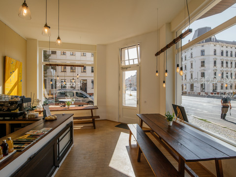 Aufnahme des geräumigen modernen Cafés sowie die angrenzenden Straßenzüge durch die große Fensterfront; Sommertag, hell, modern, kaffeehaus, cafe
