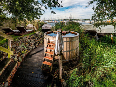 Ein Badezuber und Liegen zum Entspannen stehen in dem Außenbereich der Wellness-Einrichtung Sauna im See.