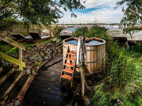Ein Badezuber und Liegen zum Entspannen stehen in dem Außenbereich der Wellness-Einrichtung Sauna im See.