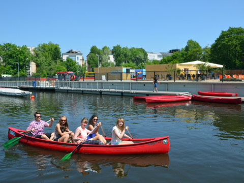 Personen paddeln in roten Ruderboten auf dem Wasser am Stadthafen Leipzig in dem neben dem Bootsverleih auch Bootsrundfahrten auf den Kanälen der Stadt wie dem Karl-Heine-Kanal angeboten werden, Wassersport in Leipzig