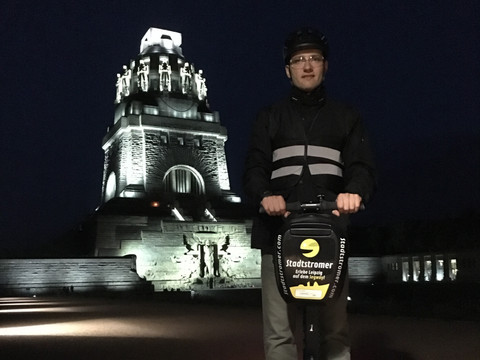 Blick auf das Völkerschlachtdenkmal Leipzig bei Nacht im Hintergrund und einen Mann auf Segway der eine Stadtführung des Erlebnisanbieters Stadtstromer besucht