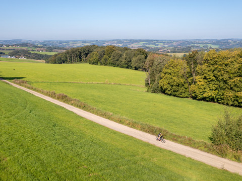 Panorama Heckberg Radfahrer auf einem Feldweg in grüner Hügellandschaft bei klarem Himmel und weitem Blick.