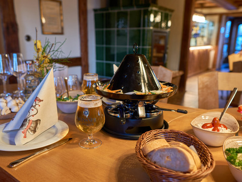 Food from the hot hat A table with a table grill full of vegetables, a glass of beer, bread basket and bowls of dips in a cozy room.