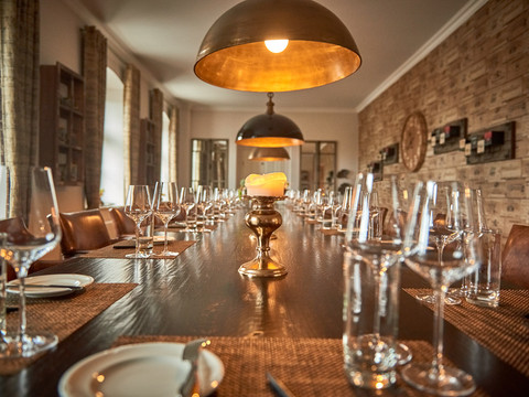 Café & Wijnhuis Koffiebranderij Schmole in Pirna Eleganter, gedeckter Esstisch mit Weingläsern und Tellern, beleuchtet von warmen, goldenen Hängelampen in einem stilvollen Raum mit Holzwänden.