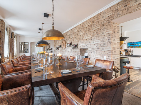 Café & Wijnhuis Koffiebranderij Schmole in Pirna Elegantes Esszimmer mit langem Holztisch, gedeckt mit Gläsern und Kerzen, umgeben von braunen Ledersesseln und beleuchtet von großen Hängelampen.