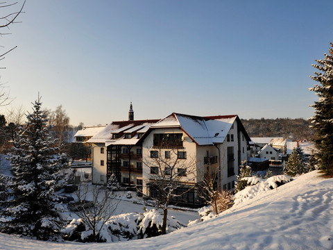 Ein großes Gebäude mit roten Dächern ist von schneebedeckten Bäumen umgeben, unter blauem Himmel bei Sonnenuntergang.