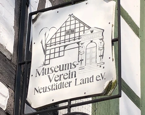 Das Bild zeigt ein Schild des Museumsvereins Neustädter Land e.V. an einem Fachwerkgebäude.