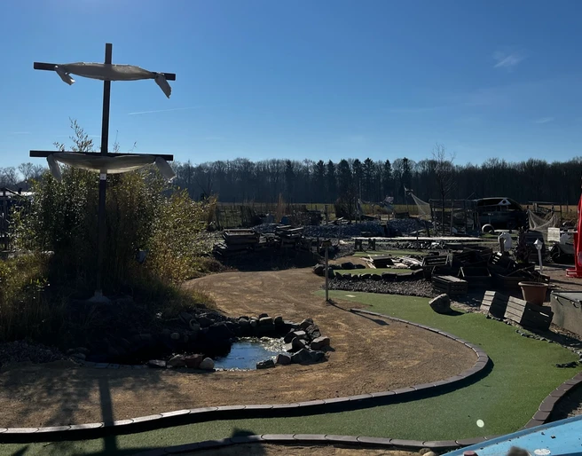 Blick auf das Gelände Activity Park Hagenburg Grünes Minigolfgelände im Activity Park Hagenburg mit Schirmen, Bänken und einem kleinen Teich.
