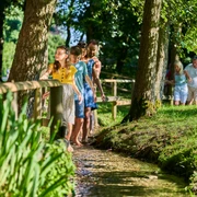 Familie auf dem Barfußpfad Eine Familie läuft barfuß durch einen Bach in einem Waldgebiet, umgeben von sommerlichen Bäumen.