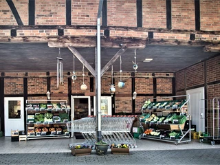 Bauckhof  Auf dem Bild ist der Eingang eines Hofladens zu sehen. Es zeigt Einkaufswagen und Regale voller frischem Gemüse.