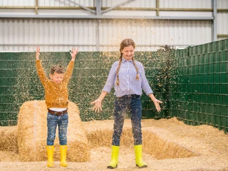 Spaß & Abenteuer auf Gut Hixholz in Velbert Zwei Kinder mit leuchtend gelben Gummistiefeln spielen fröhlich in einem Raum voller Stroh.