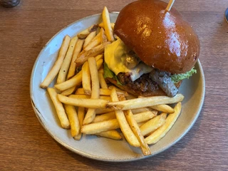 Ein Teller mit Pommes frites und einem Burger mit geschmolzenem Käse und einem glasierten Brötchen.