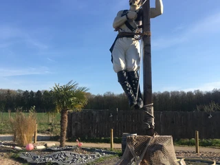 Pirat im Activity Park Hagenburg Piratenskulptur im Activity Park Hagenburg, an einem Pfahl angebunden, vor blauem Himmel und Wald.