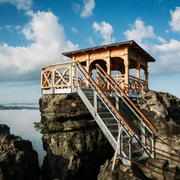 Dittersbacher Felsen Holzpavillon auf einem Felsen mit Treppe, umgeben von Nebel und blauem Himmel mit Wolken; ruhige, malerische Atmosphäre.