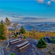 Hoher Schneeberg Zwei Holzbänke auf einem felsigen Aussichtspunkt mit Blick auf bewaldete Hügel und ein Tal unter einem klaren blauen Himmel.