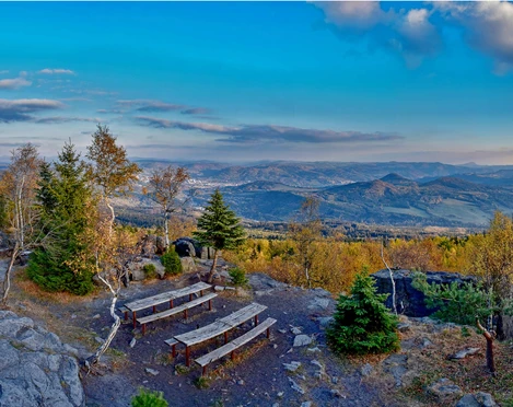 Hoher Schneeberg Zwei Holzbänke auf einem felsigen Aussichtspunkt mit Blick auf bewaldete Hügel und ein Tal unter einem klaren blauen Himmel.