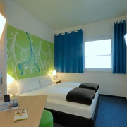 Zweibettzimmer mit modernen Möbeln, blauer Teppich, farbige Akzente und Flachbildfernseher.