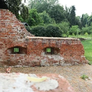 Ellerburg Rote Backsteinmauer mit Bögen steht auf bewachsenem Gelände, umgeben von dichten Bäumen und Wiesen.