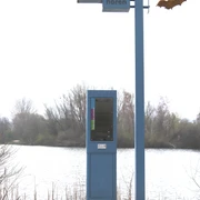 IMG_0308.JPG Blauer Audioguide-Pfahl mit "Fledermäuse hören"-Schild vor einem See, umgeben von Bäumen.
