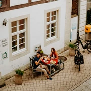Teutoburger-Wald-Brakel-Tourist-Info-┬®-Teutoburger-Wald-Tourismus-(3).jpg Zwei Personen genießen ein Essen im Freien vor einem historischen Fachwerkgebäude in Brakel.