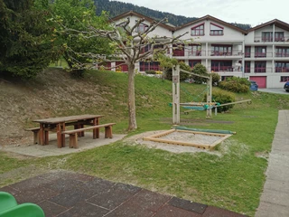 Spielplatz-Ried-Brig-Schulhaus (1).jpg Bild von Sandkasten, Wippe und TischPicture of sandbox, seesaw, and tableImage d'un bac à sable, d'une balançoire et d'une table