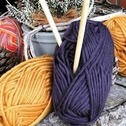 Handarbeitsgruppe.jpg Auf einem Baumstumpf liegen farbige Wollknäuel neben Stricknadeln.