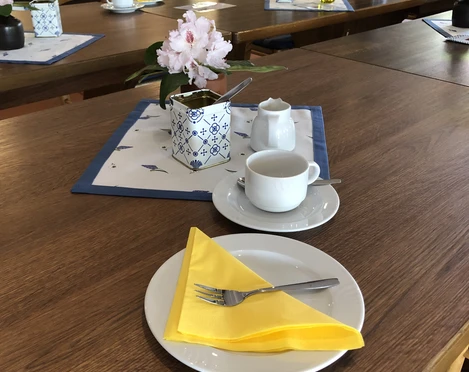 Kloencafe2.JPG Auf einem Holztisch steht ein gedeckter Tisch mit einer gelben Serviette.