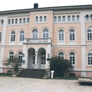 IMG_0420.JPG Ein historisches Gebäude mit rosafarbener Fassade, Bögen und vielen Fenstern auf Kopfsteinpflaster.