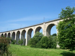 Altenbeken_Viadukt_Teutoburger Wald Tourismus_I Bohlken (1).JPG Steinviadukt mit Bögen und Gleisen, eingebettet in grüne Landschaft, blauer Himmel im Hintergrund.