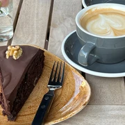 Schokokuchen Ein Stück gläserner Schokokuchen mit Walnuss auf einem Teller neben einem Cappuccino mit Herzmuster.