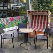 Drei Bistrostühle und ein runder Tisch stehen vor einem rot-weiß gestreiften Strandkorb auf gepflastertem Boden.