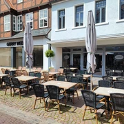 Genusswirtschaft Einladender Außenbereich eines Cafés in einer gepflasterten, sonnigen Fußgängerzone.