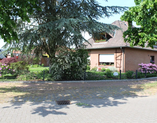 Ein rotes Backsteinhaus mit gepflegtem Garten und blühenden Sträuchern; ein einladender Ort.