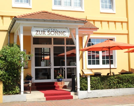 Hotel zur Sonne Der Eingang des Hotels zur Sonne mit rotem Teppich, orangenen Sonnenschirmen und Topfpflanzen.