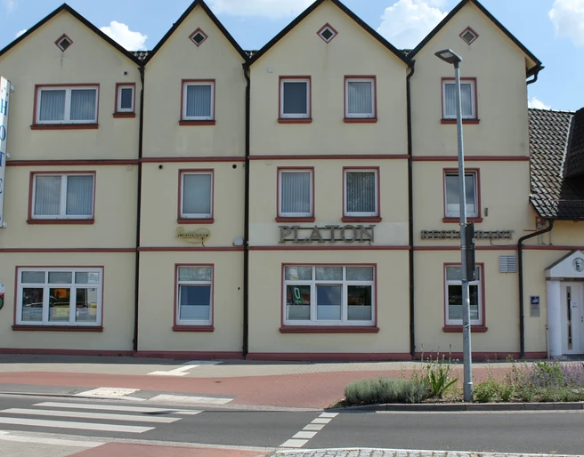 Drei-stöckiges Gebäude des Hotels Platon mit weißer Fassade und markant roten Fensterrahmen.