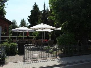 Hotel und Restaurant Ephesus am Weserwehr mit sonniger Terrasse, umgeben von grünen Bäumen.