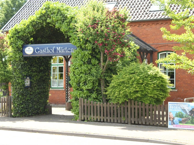 Historischer Gasthof mit üppiger Begrünung und einladendem Torbogen; rote Klinkerfassade im Hintergrund.