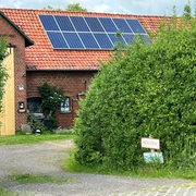 Keramik Winzlar Das Bild zeigt ein rotes Backsteingebäude mit Solarpaneelen auf dem Dach, umgeben von grüner Vegetation.