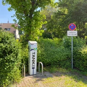 Ladesäule Kölner Straße Ladesäule für Elektrofahrzeuge zwischen grünen Hecken, daneben Parkverbots- und Reserviert-Schild.