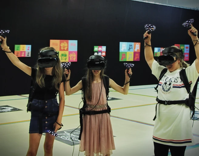 7th Space VR Langenfeld Drei Personen in virtueller Realität mit Headsets und Controllern in einem Indoor-Areal.