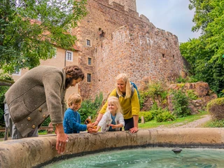 Burg Gnandstein - Sehenswürdigkeiten in der Leipzig Region Blick auf die imposante Burg Gnandstein, im Vordergrund spielt eine Familie am Burgbrunnen mit dem Wasser, Familie, Freizeit, Kinder, Ausflug