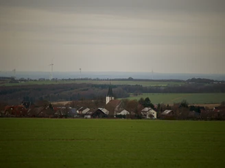 Dorfansicht von Dörenhagen mit Kirchturm im Zentrum, umgeben von sanften Hügeln und Windkraftanlagen.